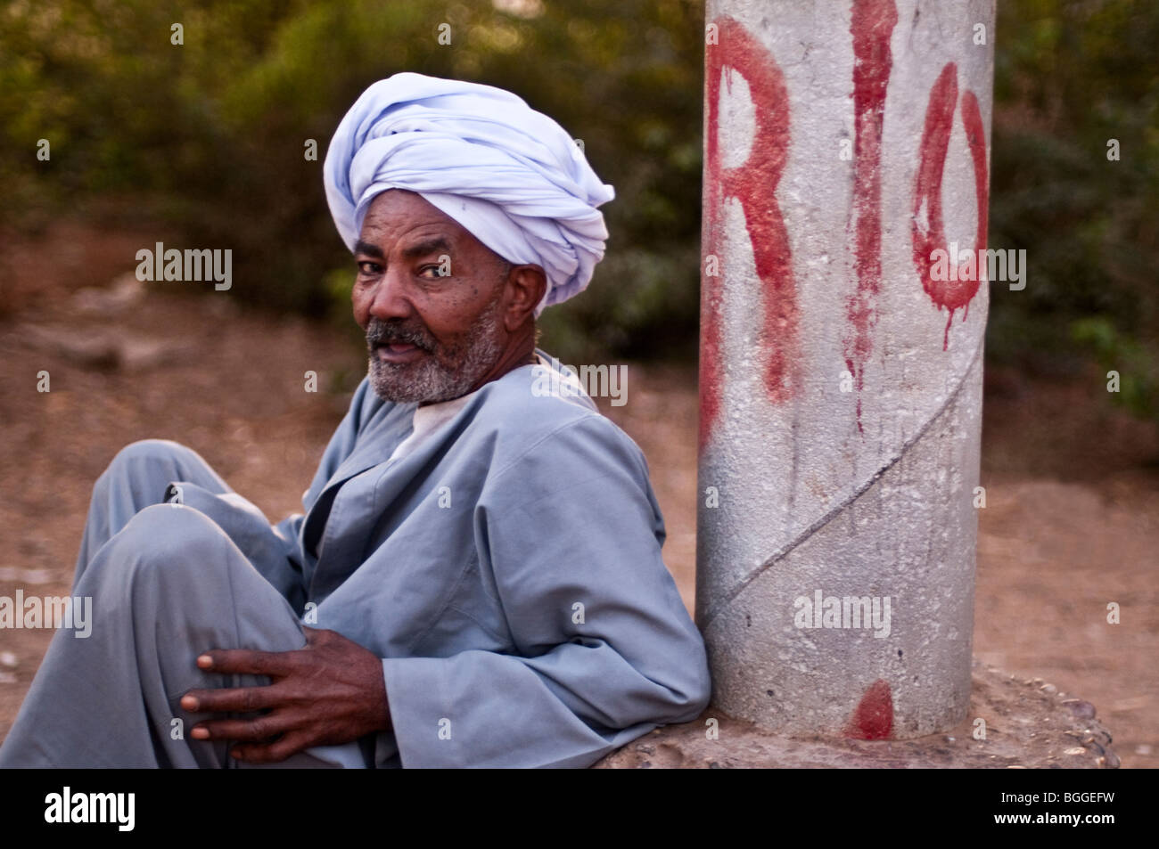 Egiziano Turbaned uomo seduto sul lato di una strada lungo il fiume Nilo. Foto Stock