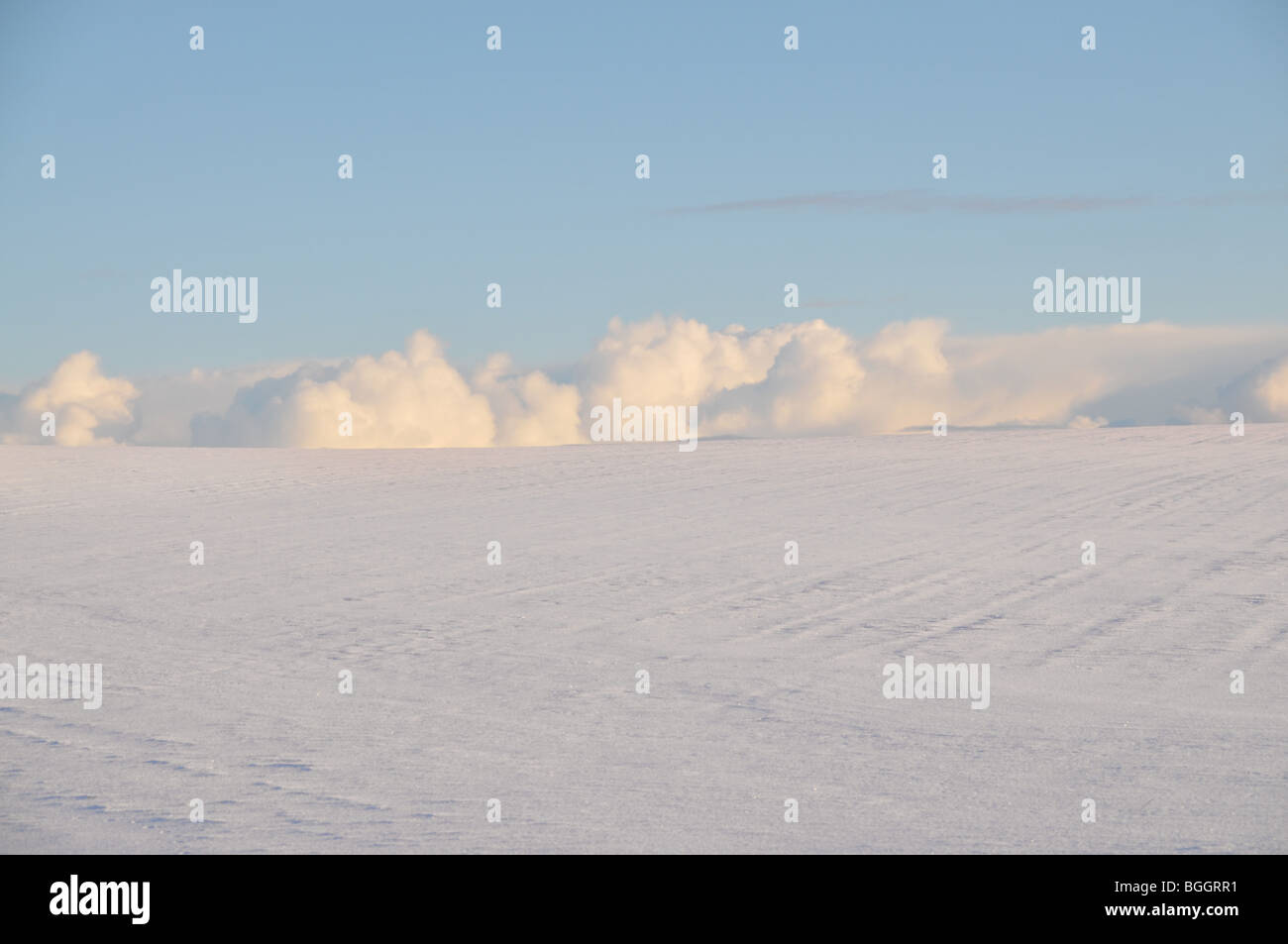 Un blu cielo invernale con un banco di nuvole sbirciare dietro i campi innevati. Foto Stock