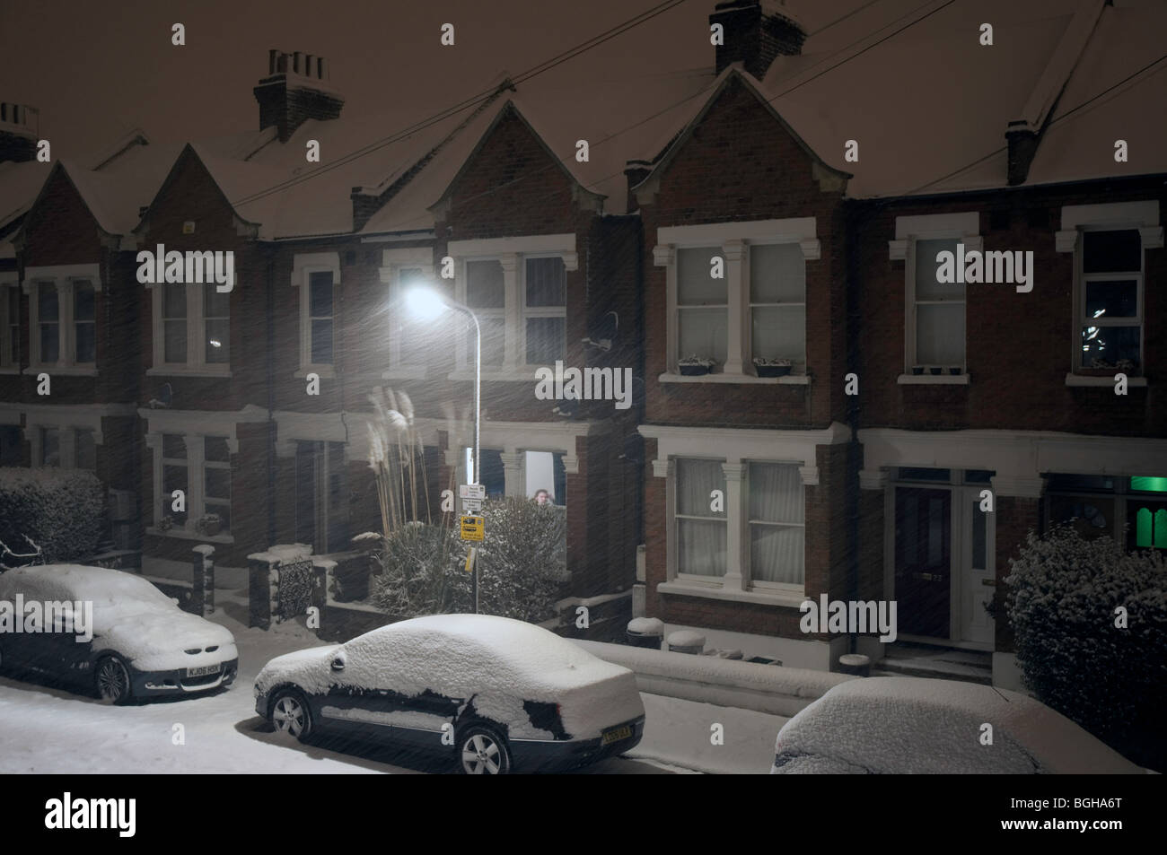 Le auto e le case nella strada di confine, Colliers Wood, a sud-ovest di Londra, coperto di neve profonda di notte Foto Stock