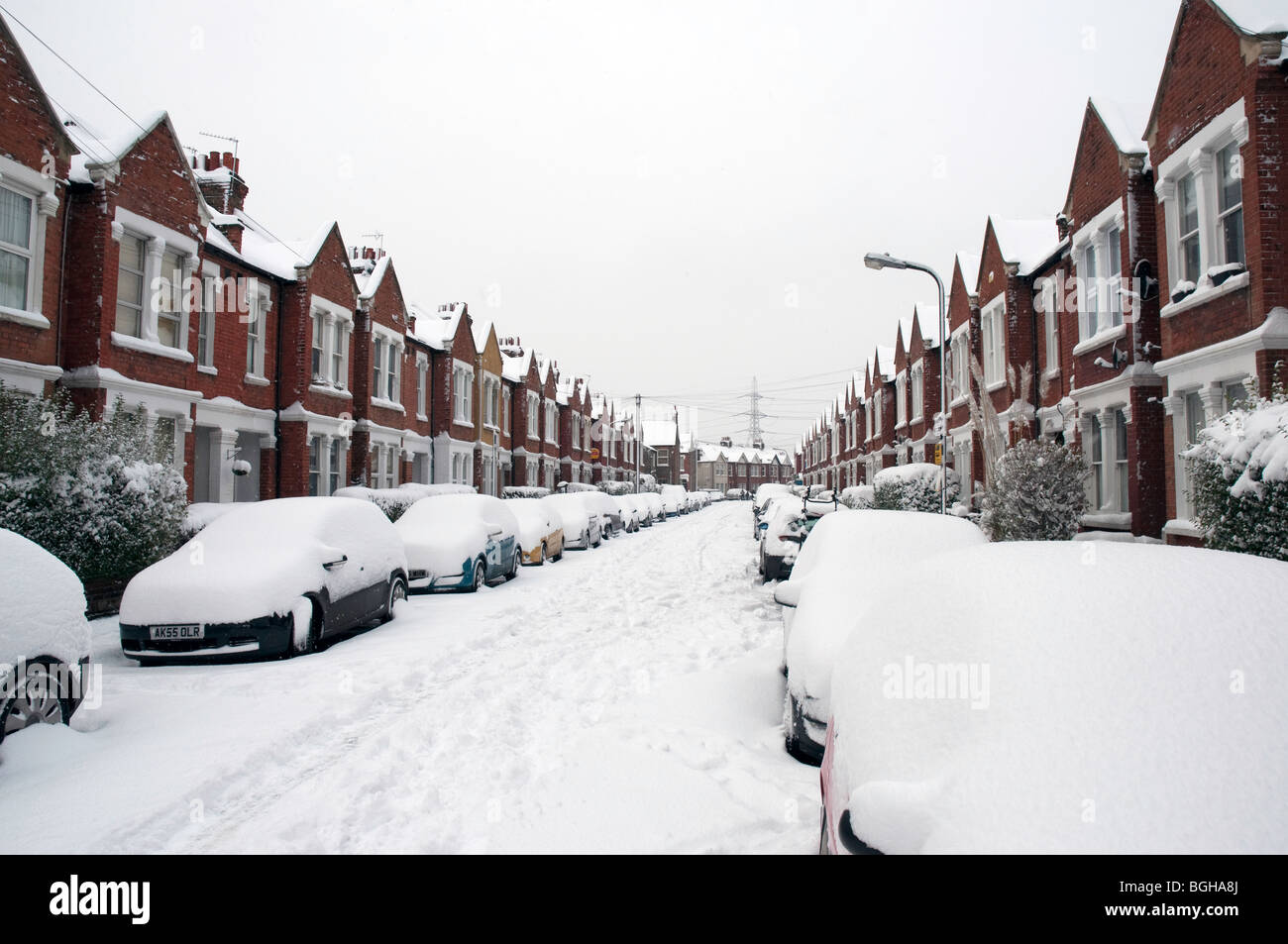 La linea di automobili e case in Boundary Road, Colliers Wood, a sud-ovest di Londra, coperto di neve profonda Foto Stock