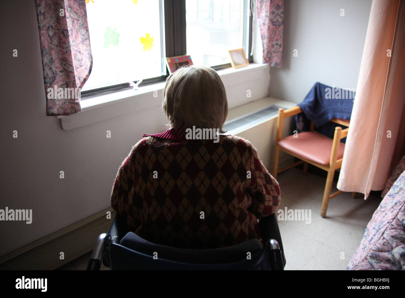 Donna anziana si siede nella sua stanza in una casa di cura guardando fuori dalla finestra, perso nel pensiero. Foto Stock