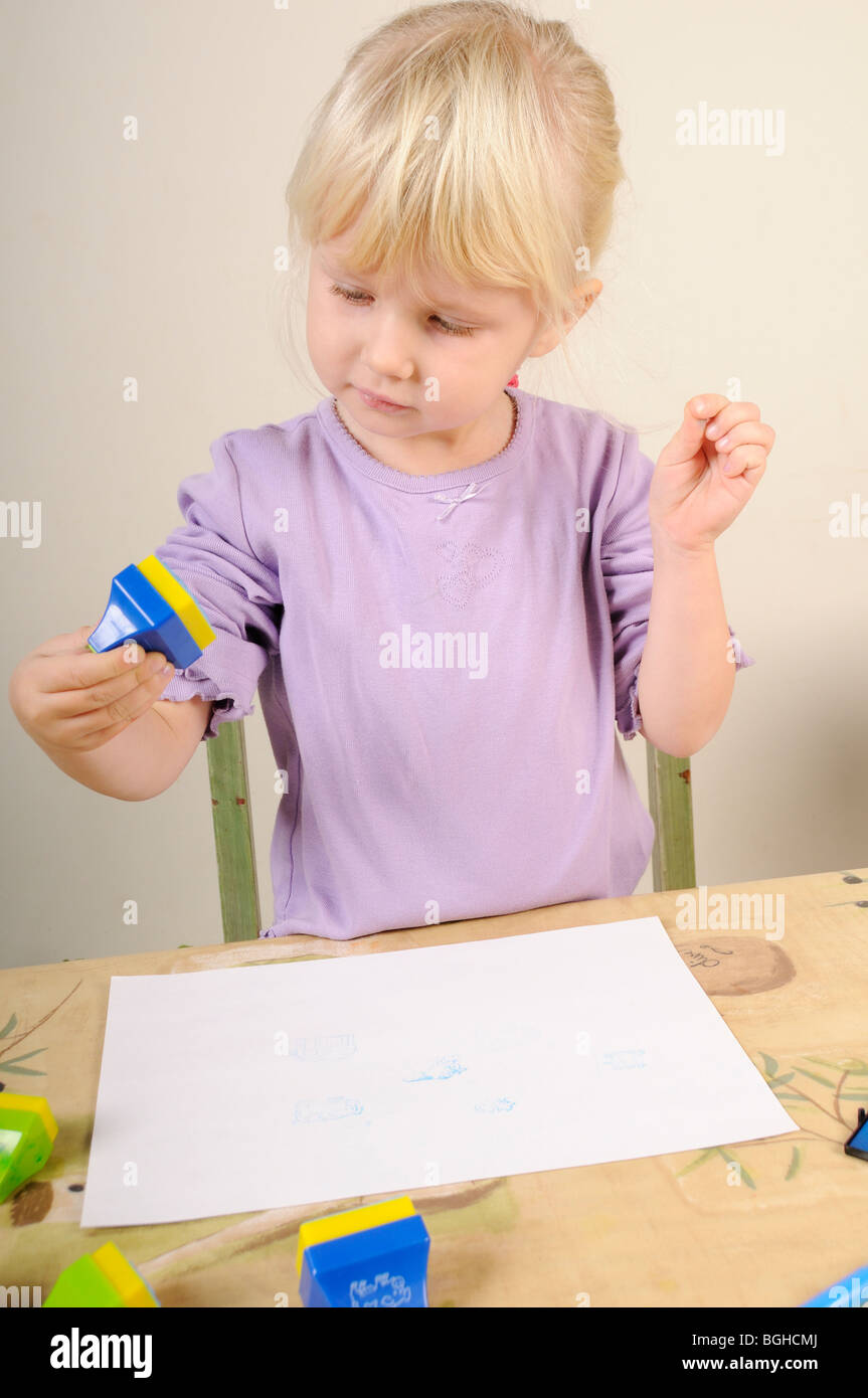 Foto di stock di un 4 anno vecchia ragazza utilizzando inchiostro timbri durante un gioco creativo sessione. Foto Stock