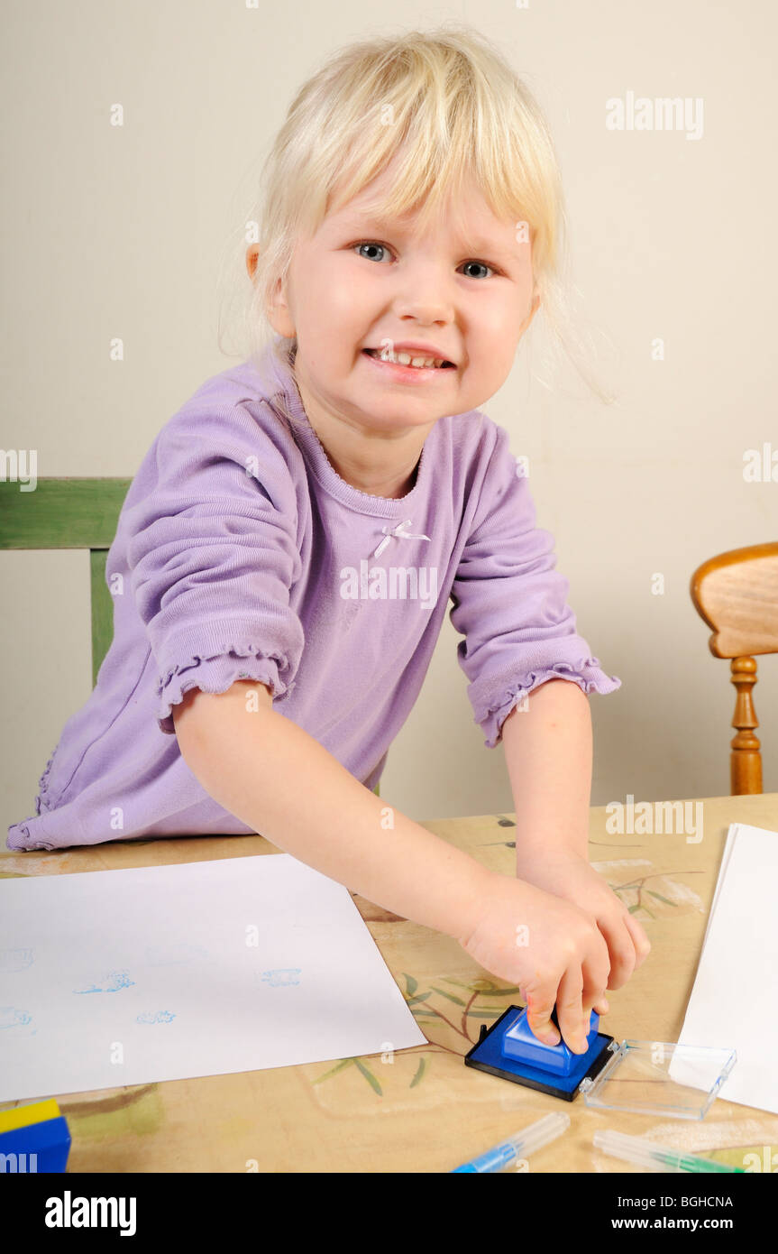 Foto di stock di un 4 anno vecchia ragazza utilizzando inchiostro timbri durante un gioco creativo sessione. Foto Stock