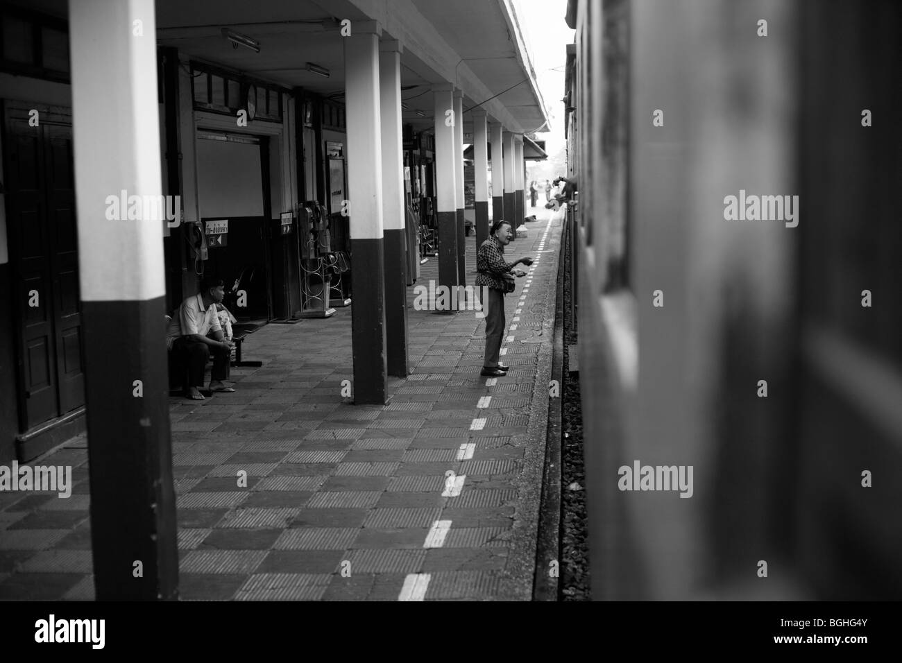Una donna vende cibo dalla piattaforma della stazione di un passeggero su un treno in Thailandia Foto Stock