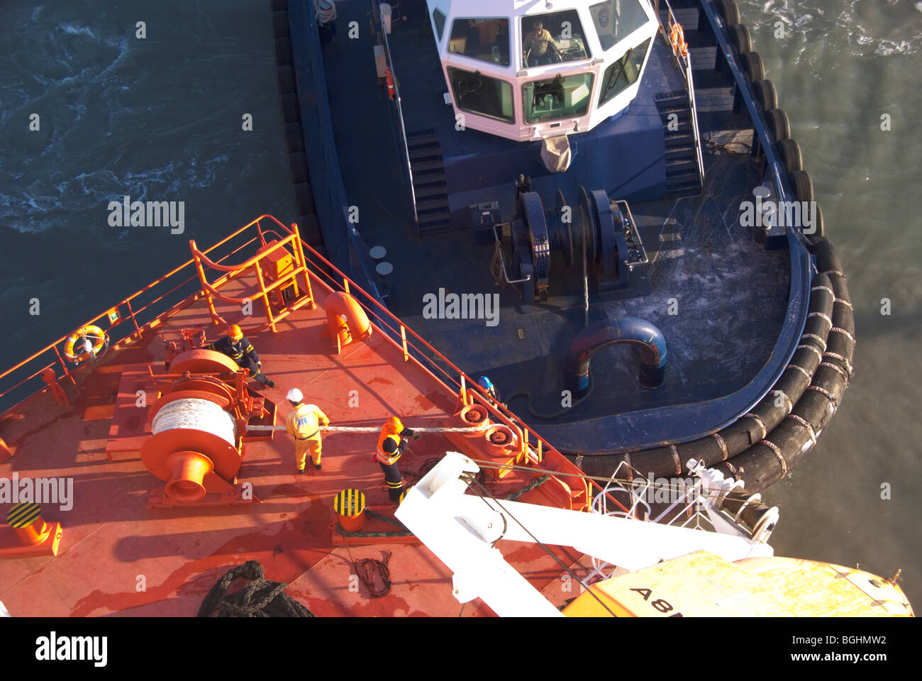 I membri dell'equipaggio di gestire linee di ormeggio mentre un rimorchiatore attende al di sotto di esse a poppa della nave. Foto Stock
