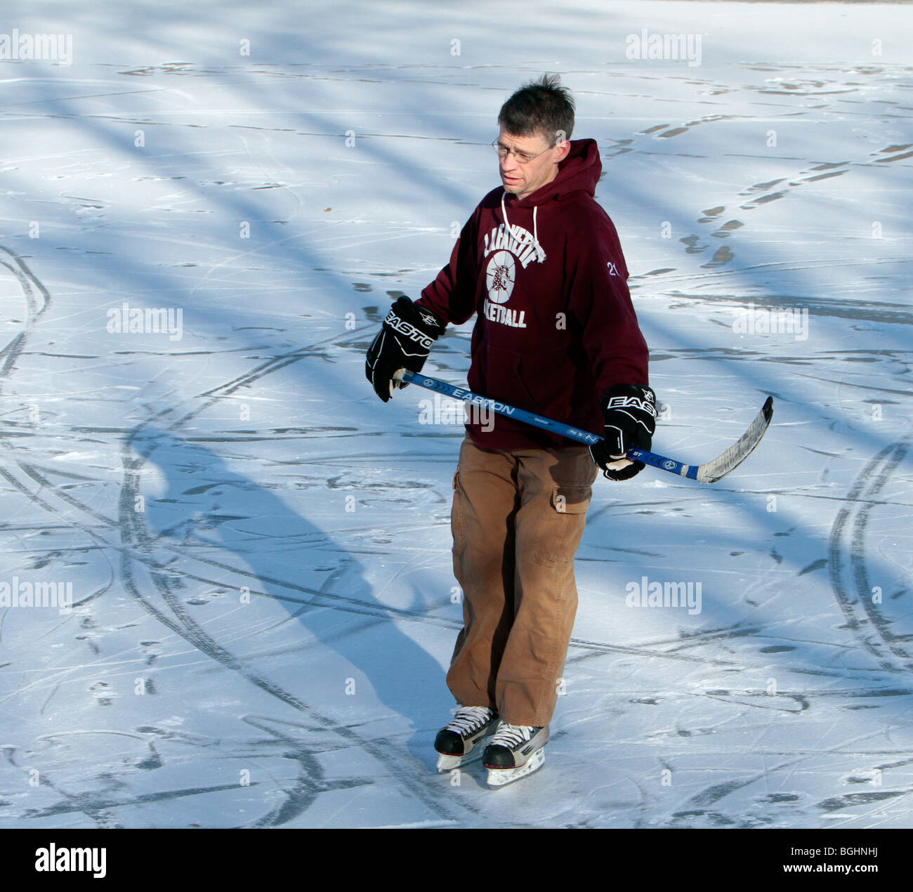 Un giovane uomo di pattinaggio sul ghiaccio. Indossa i pattini da hockey ha una mazza da hockey e hockey Guanti a. Il ghiaccio ha un rivestimento di neve. Foto Stock