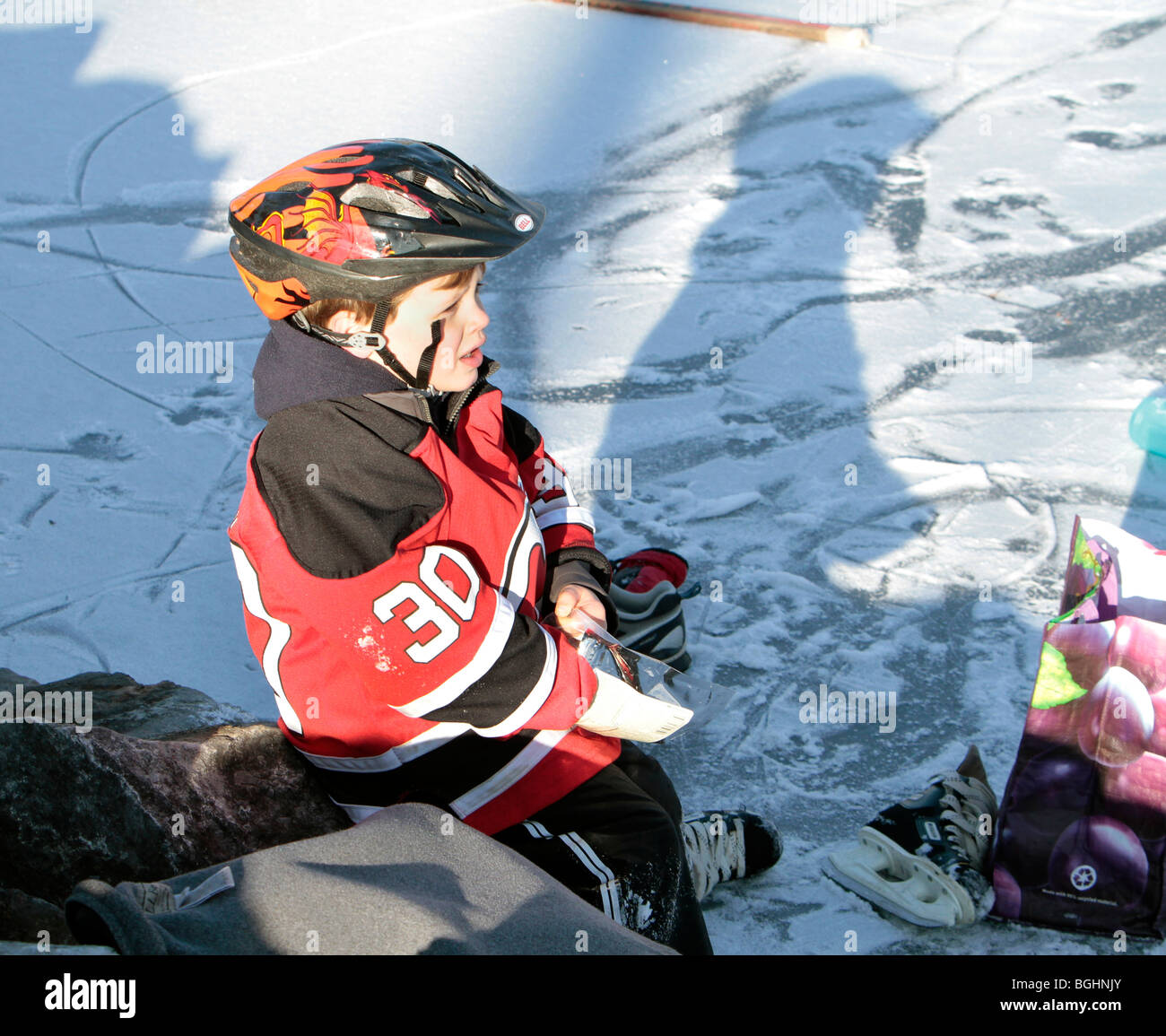 Un giovane maschio bambino vestito in New York diavoli ingranaggio di hockey su ghiaccio con il suo casco stick puck ma nessun pattini. Foto Stock