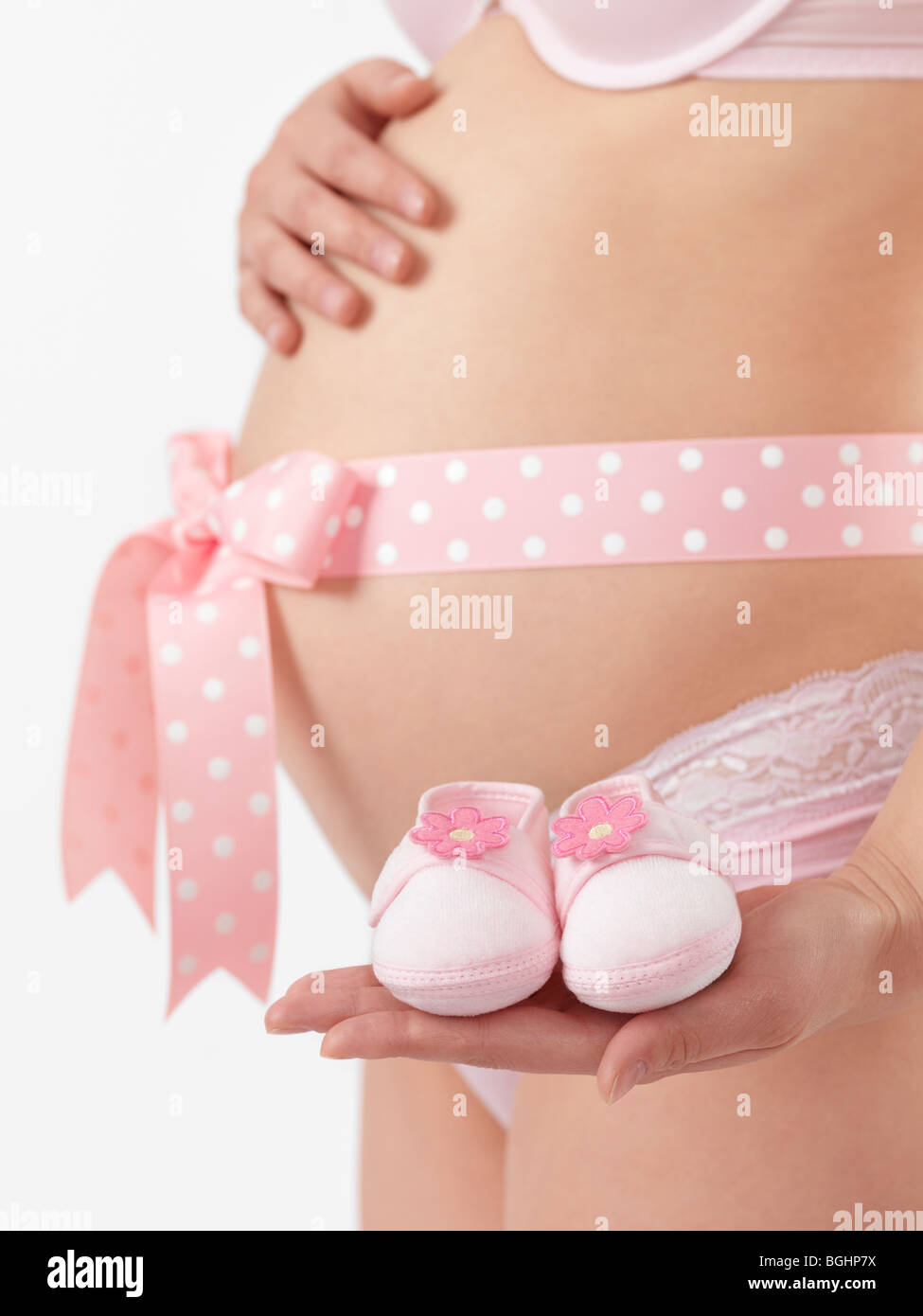 Donna incinta con un fiocco rosa sul suo ventre azienda scarpe per bambini  in mano Foto stock - Alamy