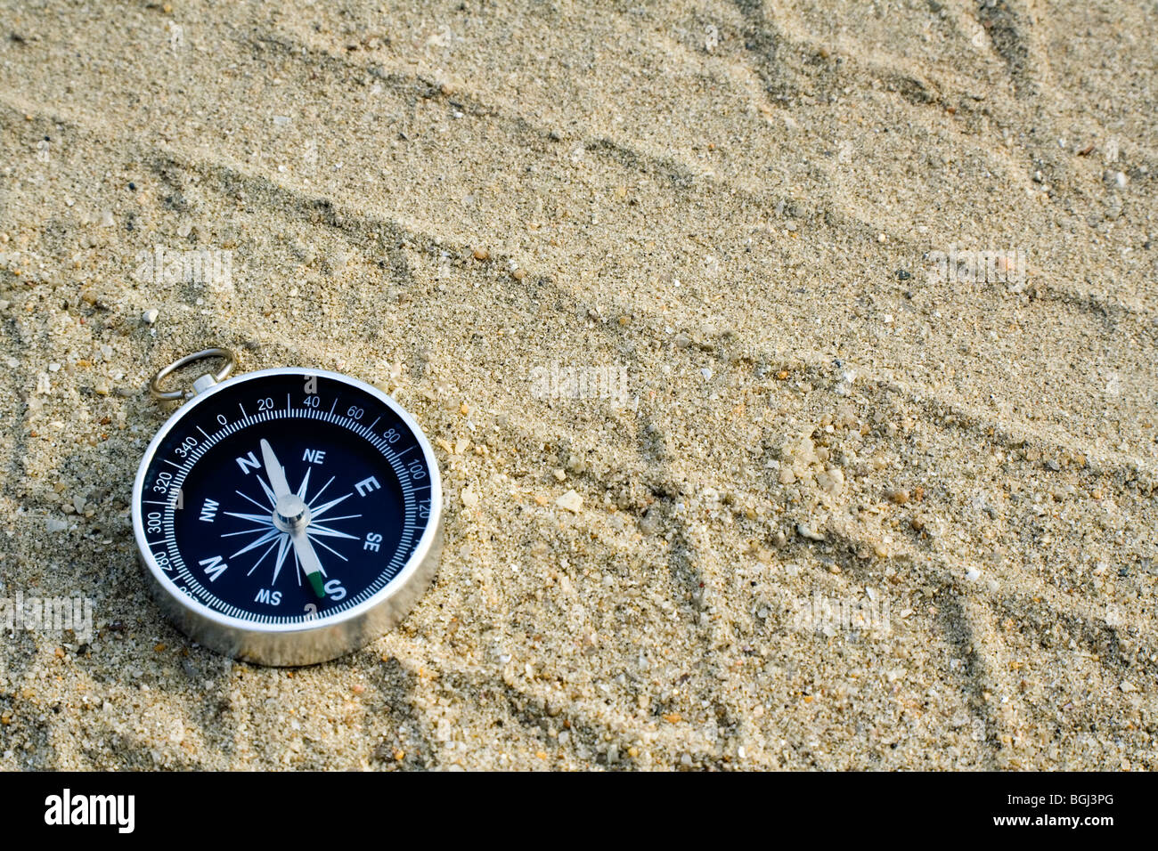 Closeup of a compass laying on a sand track Foto Stock