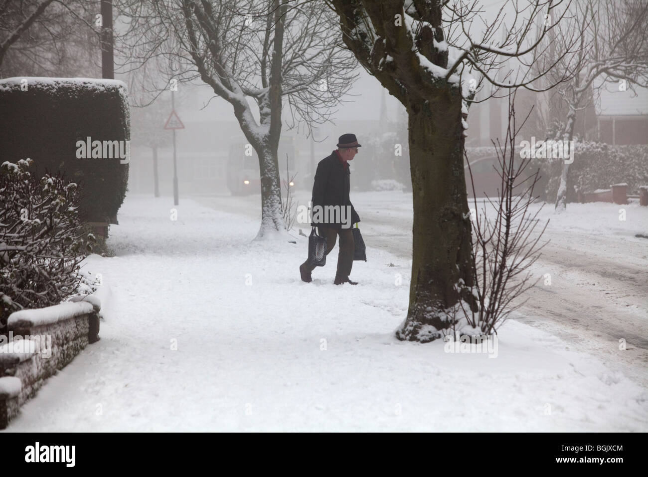 Un uomo anziano lotte attraverso la neve con le borse della spesa in Redditch, Worcestershire, Regno Unito Foto Stock