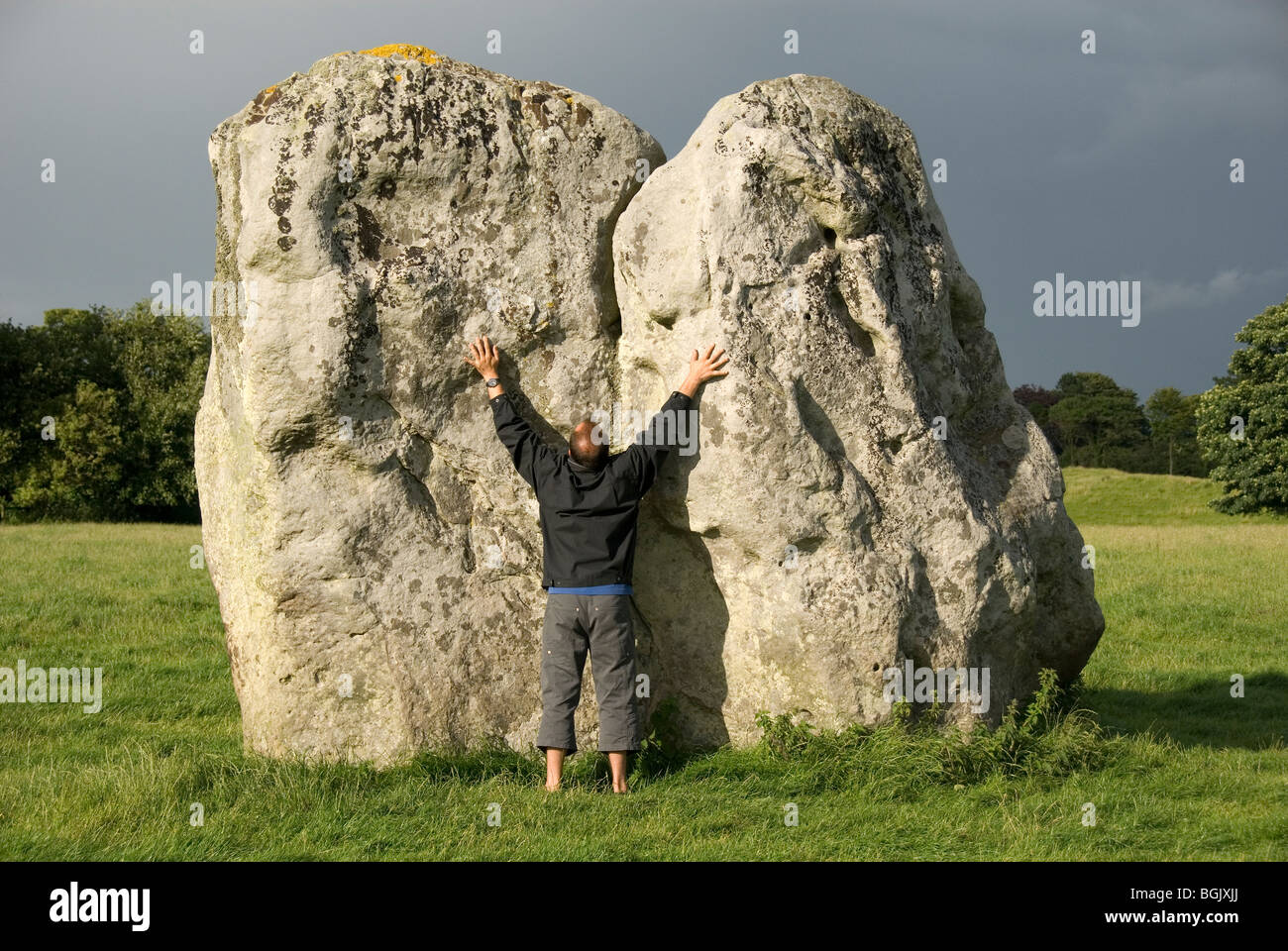 Uomo di toccare un grosso masso, le braccia tese, cerchio di pietra, Avebury, Wiltshire, Inghilterra, Gran Bretagna, Europa Foto Stock