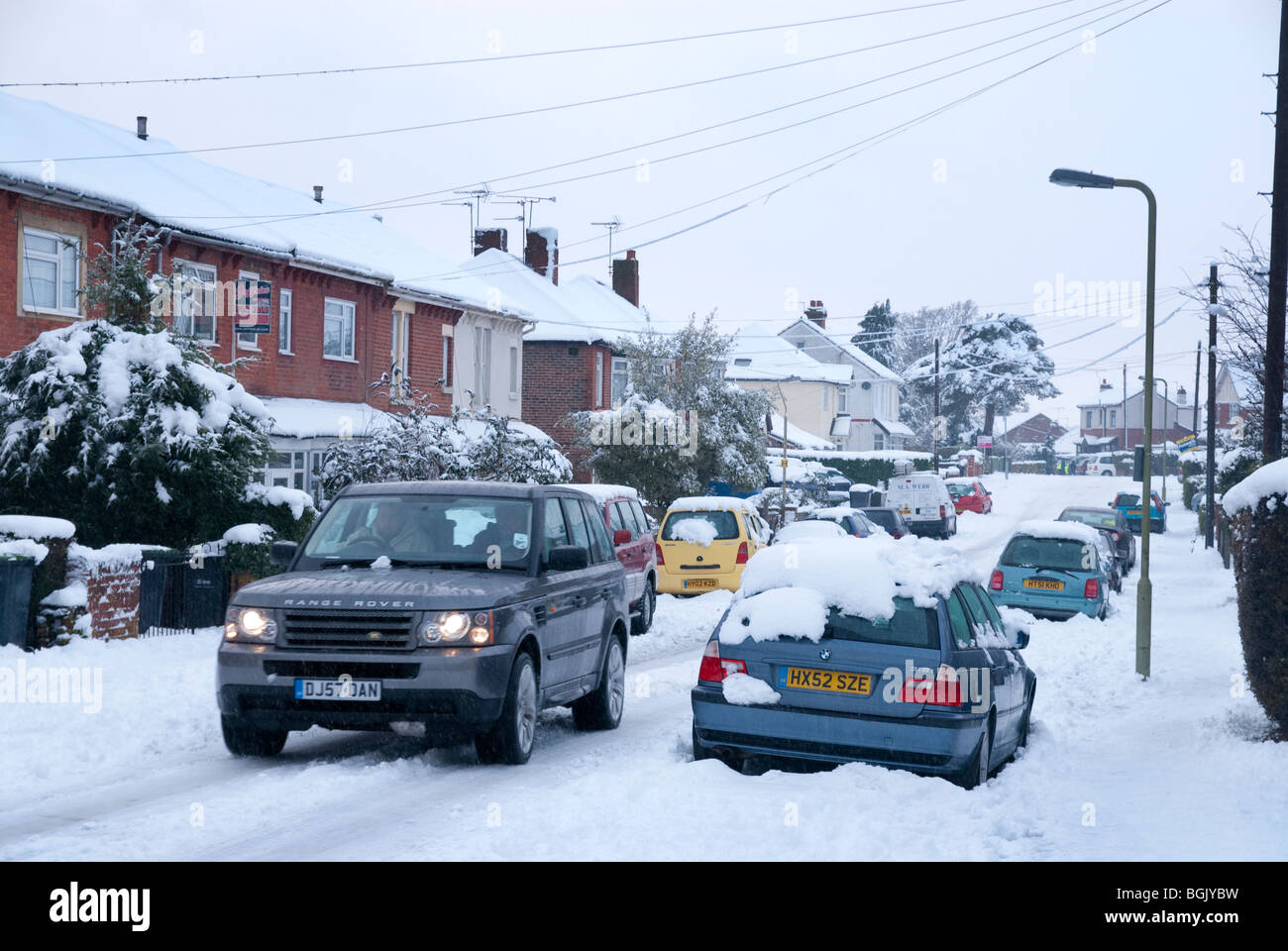4x4 passando parcheggiata coperta di neve i veicoli su terreni innevati strada laterale. Grande neve caduta A3 area di hampshire gennaio 2010 Foto Stock