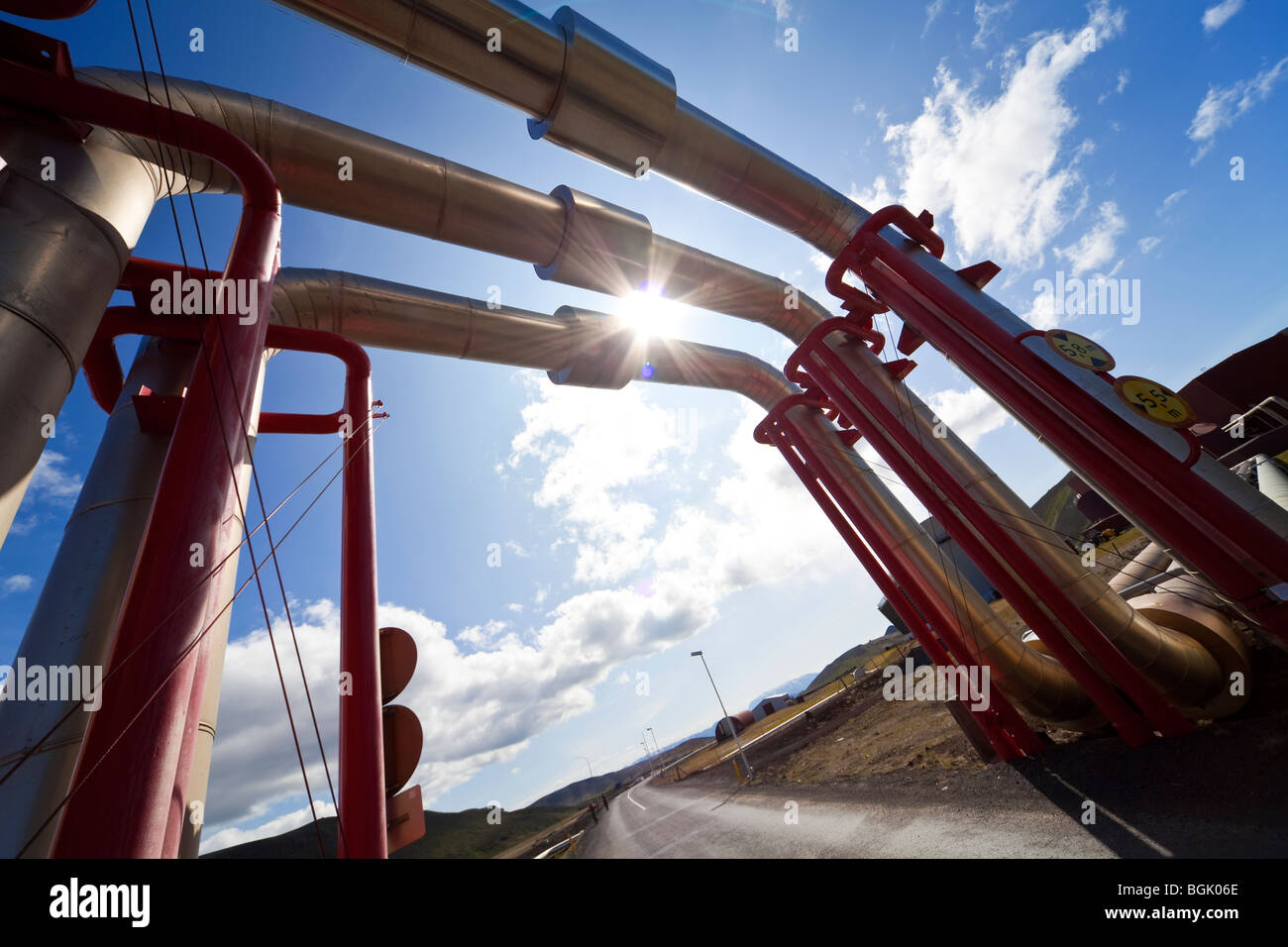 Tubi industriali e la tubazione deviata verso l'alto e su una strada per consentire il passaggio di traffico al di sotto. Girato in location in Islanda. Foto Stock