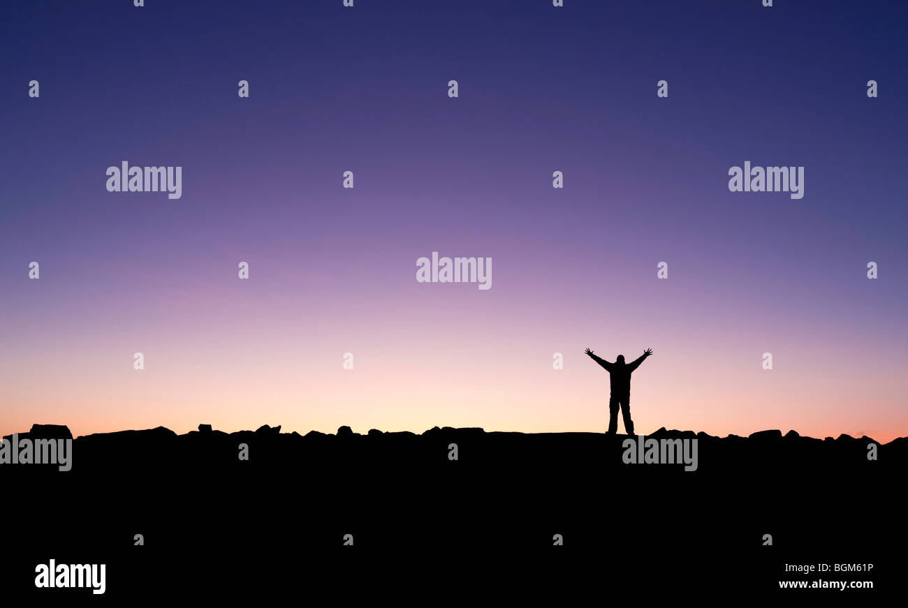Silhouette di un uomo alzando le mani nel sunrise dopo la conquista di un vertice Foto Stock