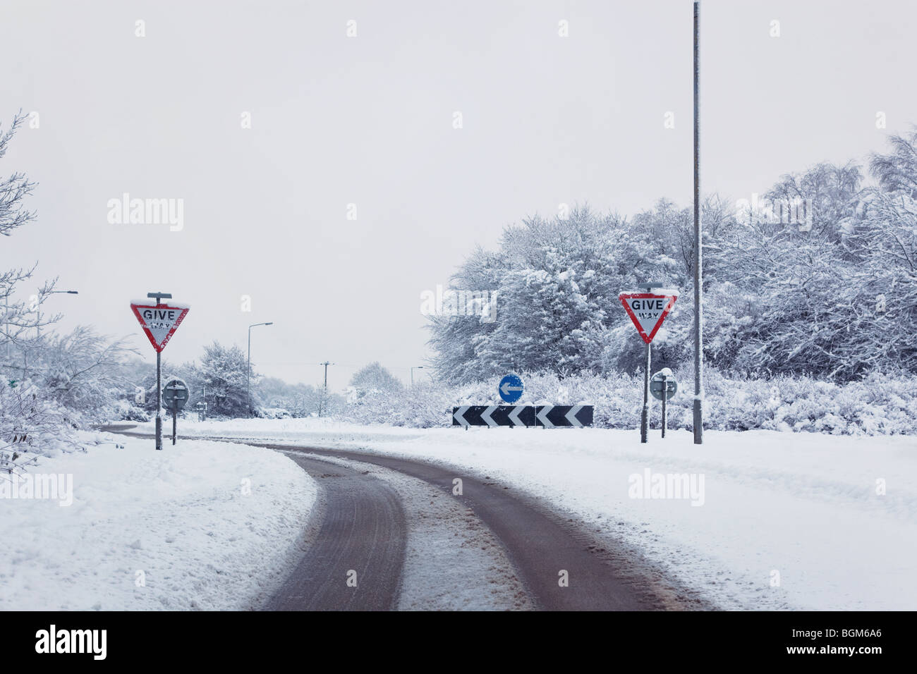 Colpo di una strada su un approccio alla rotatoria dopo un pesante la caduta di neve, dare modo segni Foto Stock