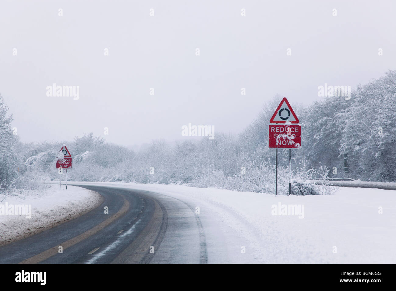 Strada con il ridurre la velocità adesso firma durante la caduta di neve dell'inverno 2010 Foto Stock