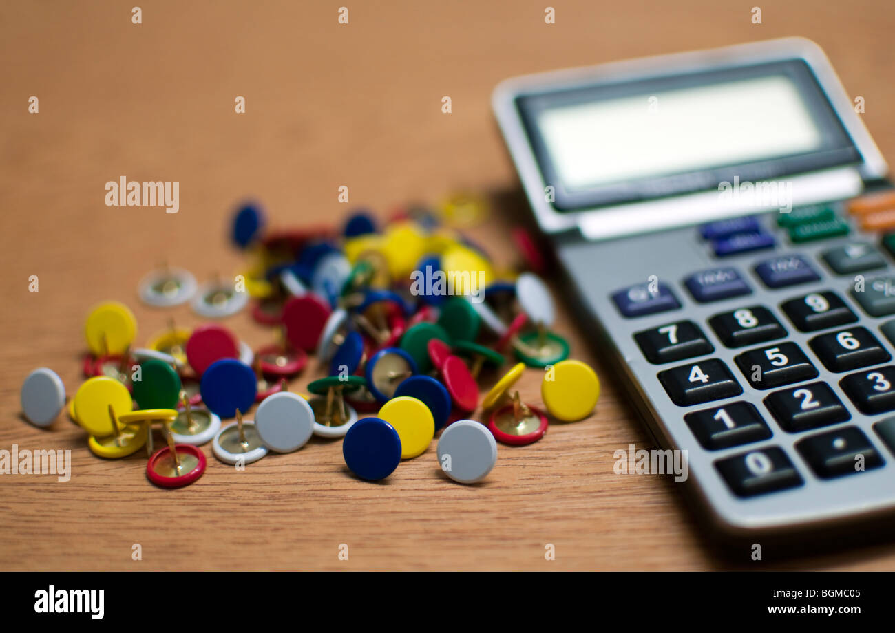 Close up della calcolatrice con variopinte puntine da disegno seduto su una scrivania Foto Stock