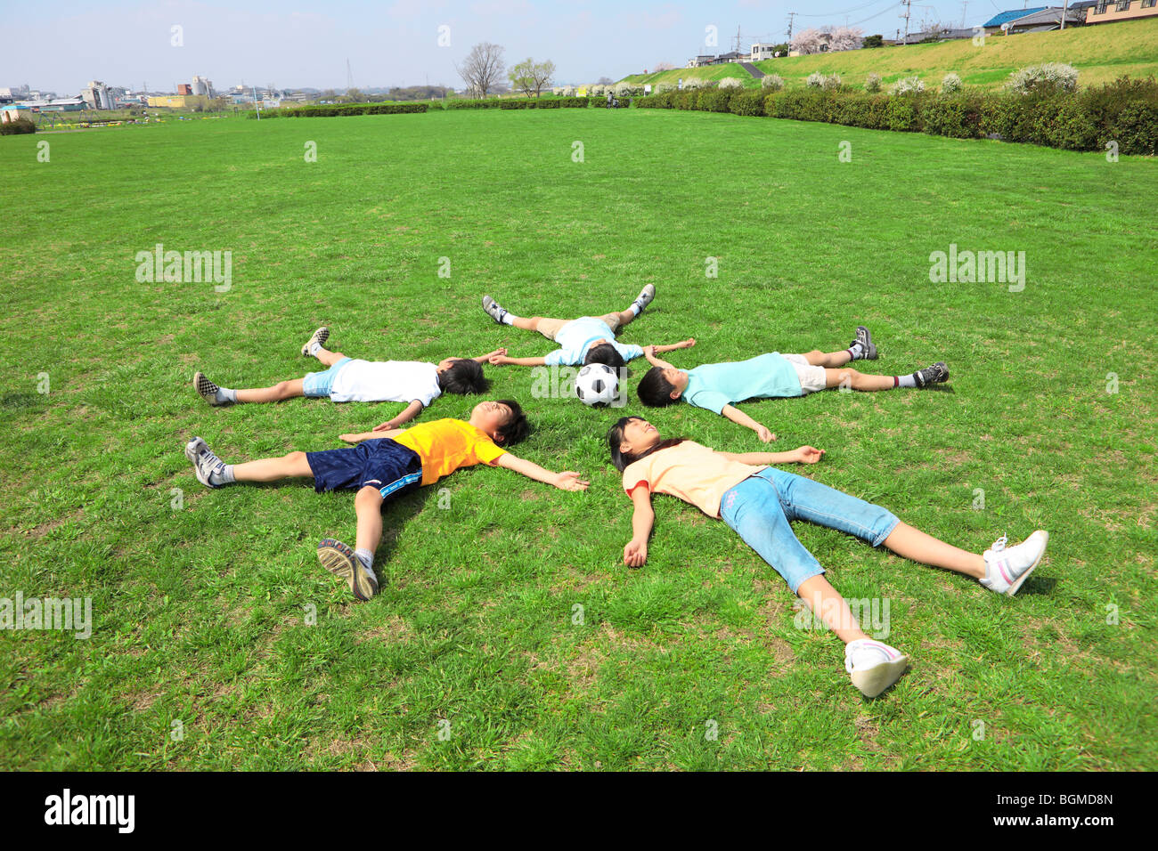 Bambini giacente sul campo con il pallone da calcio. Futako-tamagawa, Setagaya-ku, Prefettura di Tokyo, Giappone Foto Stock