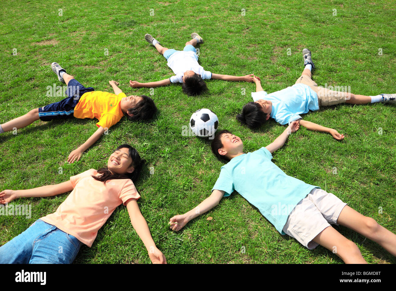 Dei bambini felici giacente sul campo con il pallone da calcio. Futako-tamagawa, Setagaya-ku, Prefettura di Tokyo, Giappone Foto Stock