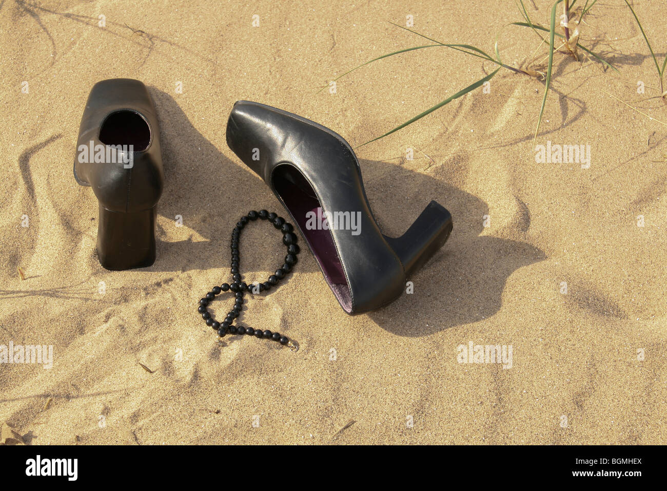 Scarpe nere e collana abbandonato su una spiaggia di sabbia Foto Stock