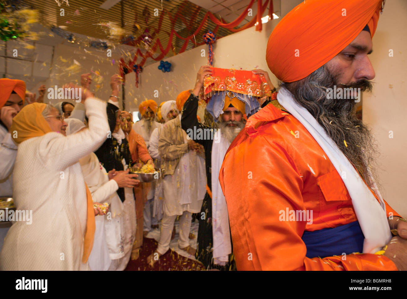 Le donne di gettare petali di fiori come il Guru Granth Sahib è portato dalla sala culto per la processione Vaisakhi Foto Stock