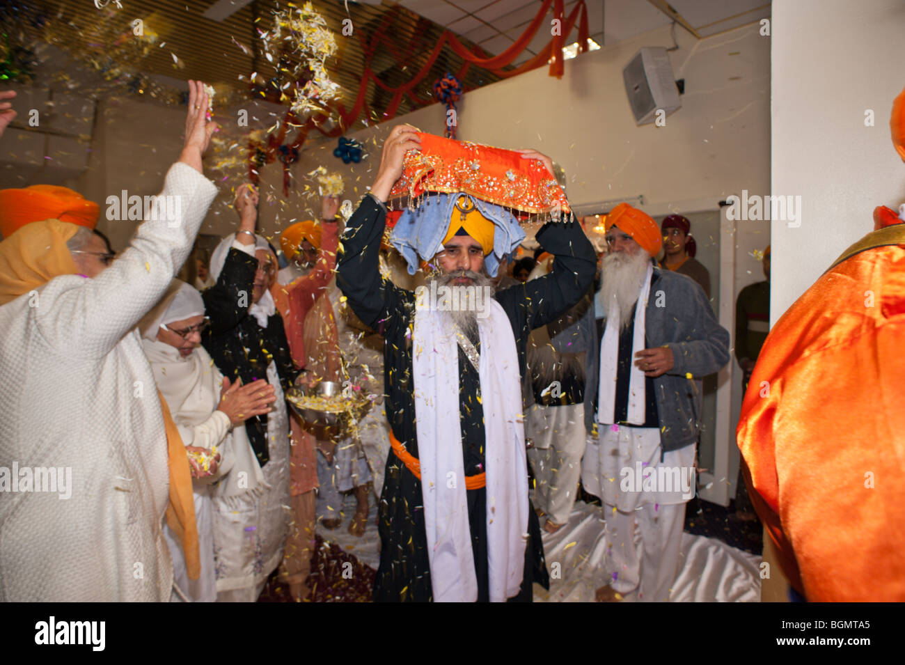 Le donne di gettare petali di fiori come il Guru Granth Sahib è portato dalla sala culto per la processione Vaisakhi Foto Stock