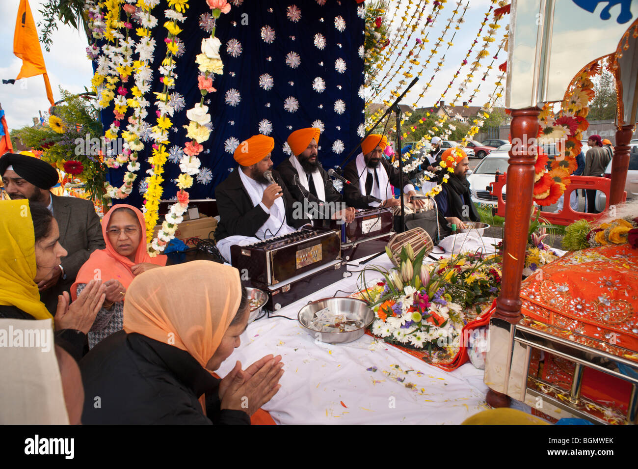 Pregando le donne, musicisti e regali di fronte al trono per Guru Granth Sahib in processione Vaisakhi, Slough Foto Stock