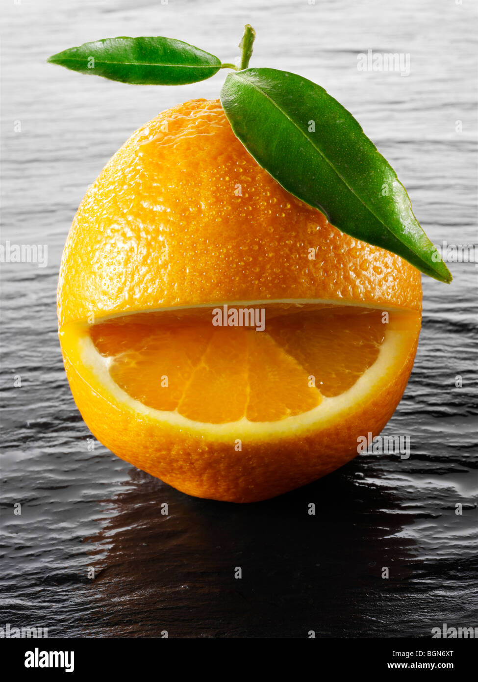 Wole arance con una faccina sorridente con foglie su sfondo nero Foto Stock