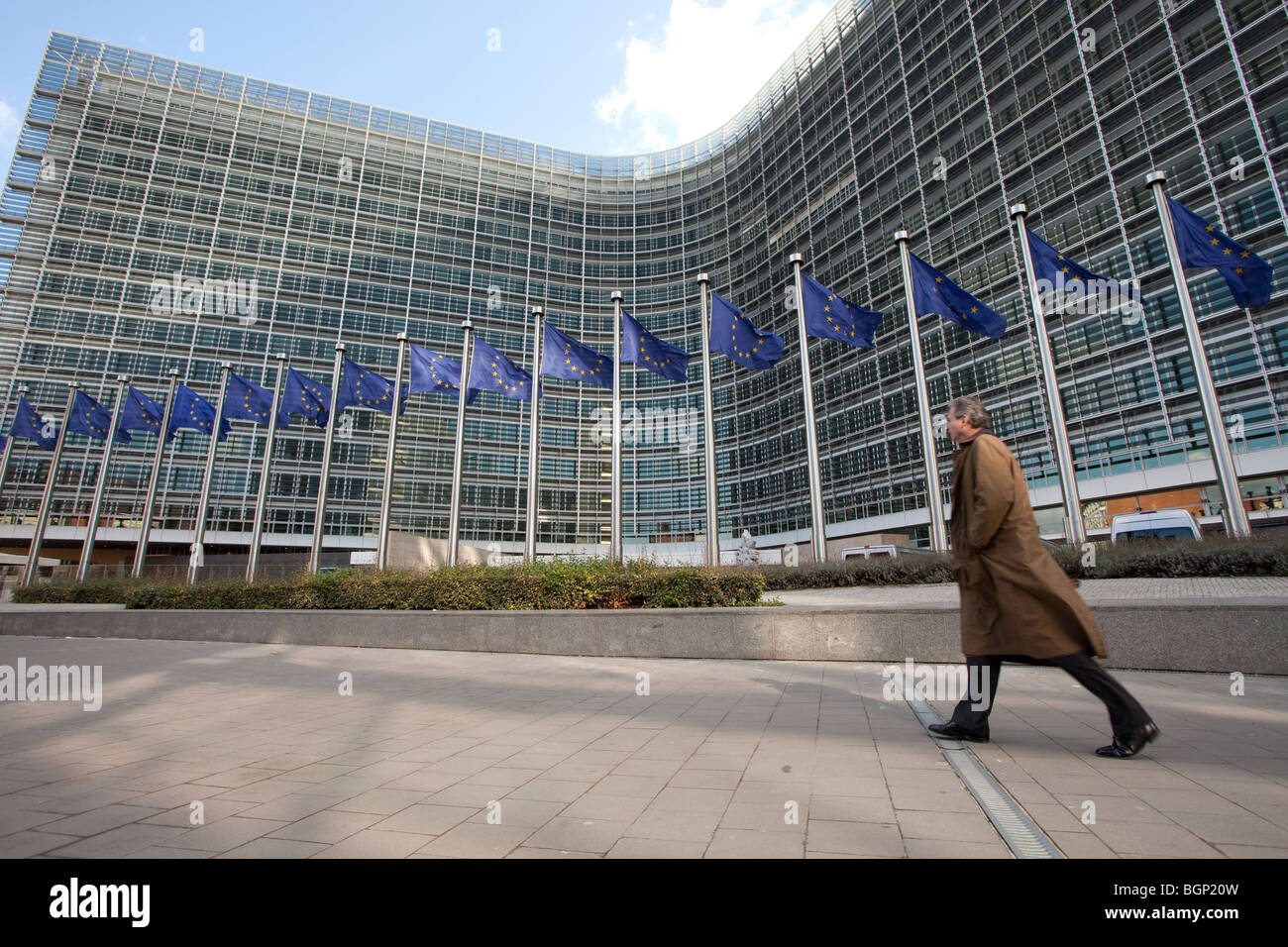 Un uomo cammina accanto alla bandiere europee al di fuori dell'edificio Berlaymont, la sede centrale della Commissione europea a Bruxelles Foto Stock