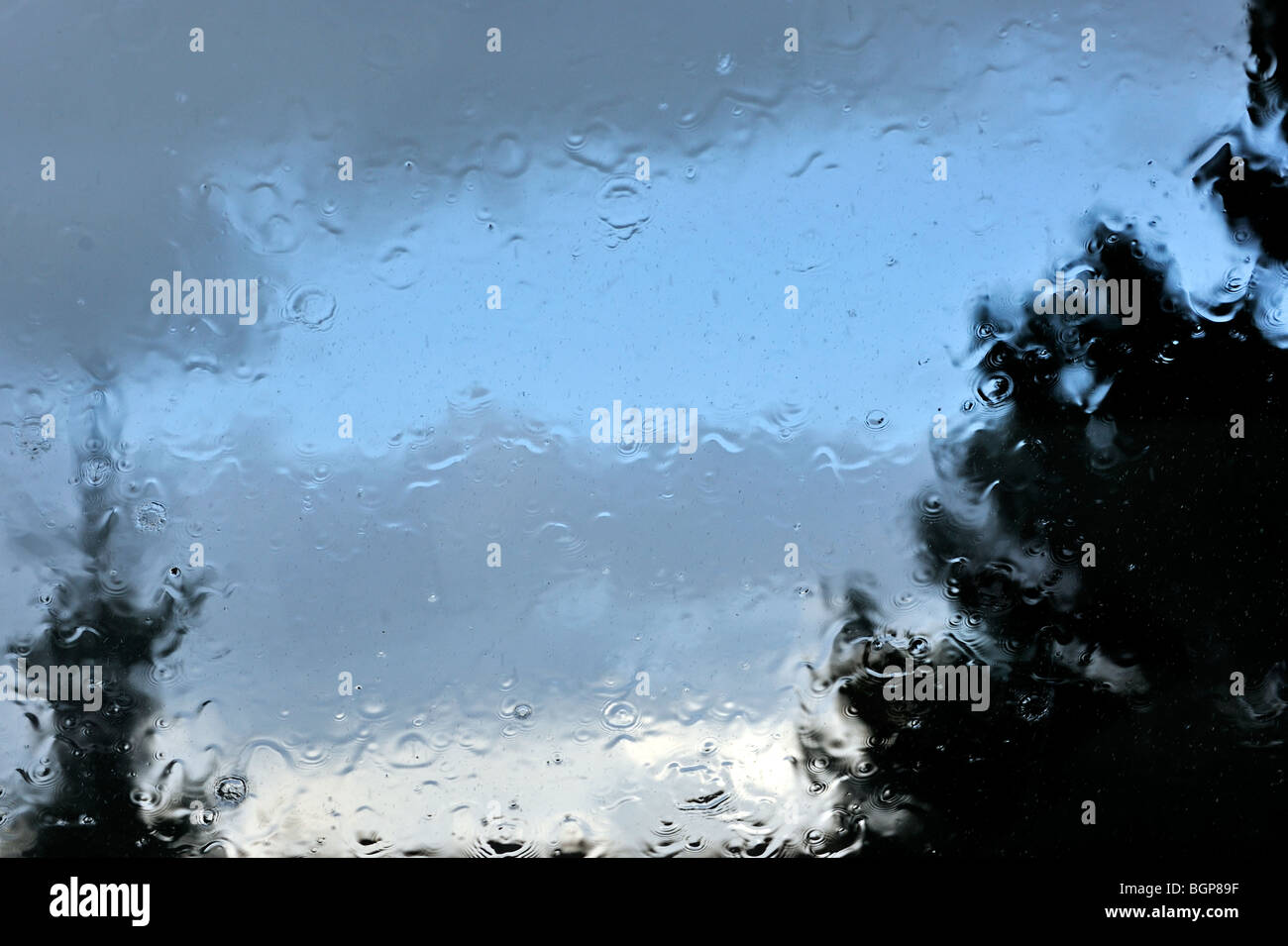 Gocce di pioggia pesante gli spruzzi di acqua sul vetro durante il diluvio e sagome di alberi Foto Stock