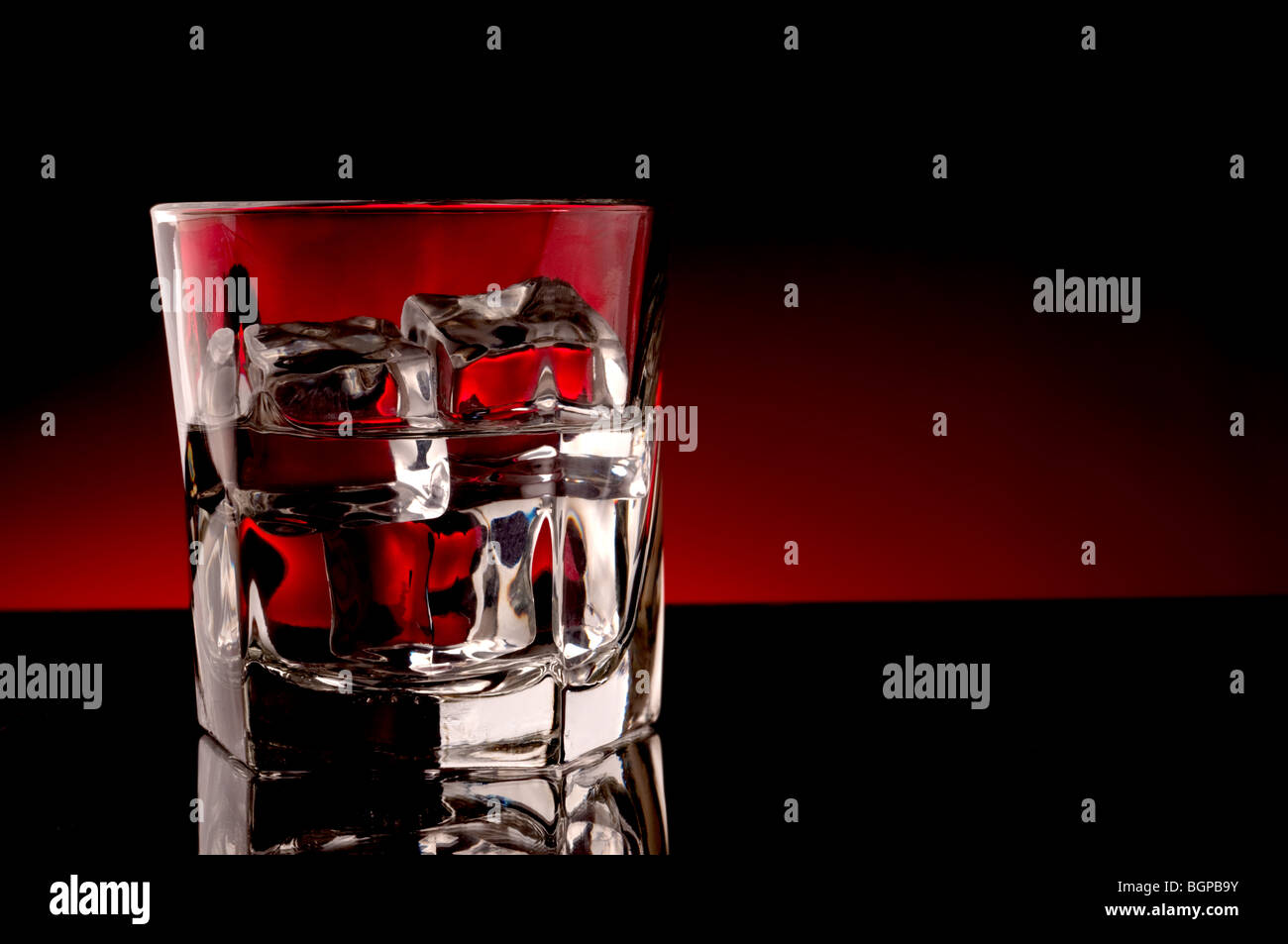 Ghiaccio e un drink in un bicchiere con un bagliore rosso sfondo Foto Stock
