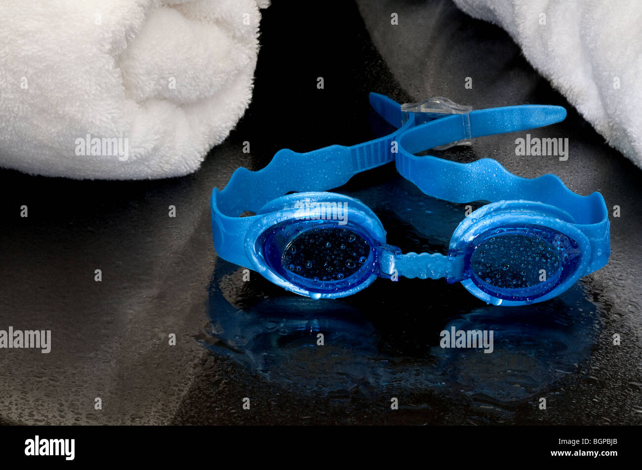 Wet occhiali da nuoto e asciugamani su una superficie riflettente Foto Stock