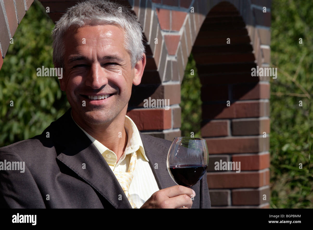 Enologo tenendo un bicchiere di vino rosso davanti al muro di mattoni nella sua vigna Foto Stock