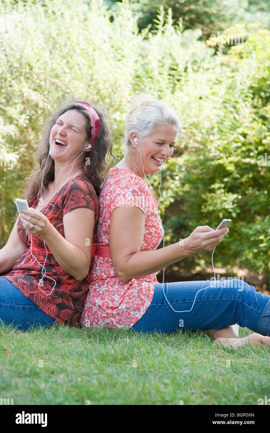 Profilo laterale di due donne mature seduta di schiena in un parco e ascolto di lettori MP3 Foto Stock