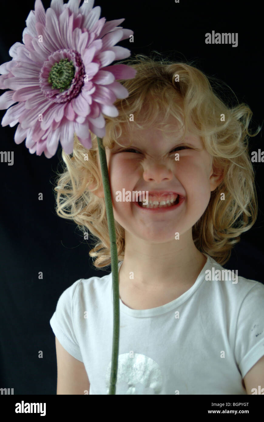 Una bimba bionda sorridente, tenendo un grande fiore rosa accanto alla sua  testa Foto stock - Alamy