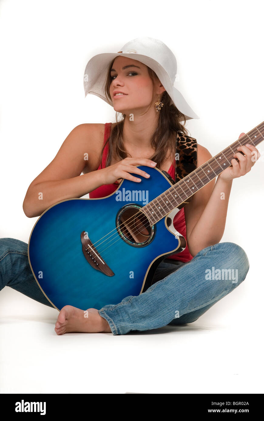 Una giovane ragazza in jeans, tenendo una chitarra e indossando rifugio bianco Foto Stock