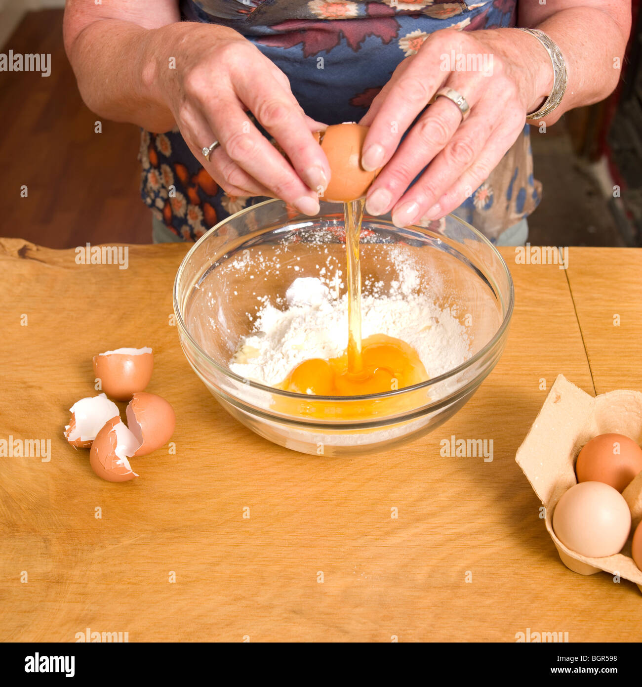 Le donne le uova di cracking nel recipiente di miscelazione di farina con le uova guscio accanto alla ciotola Foto Stock