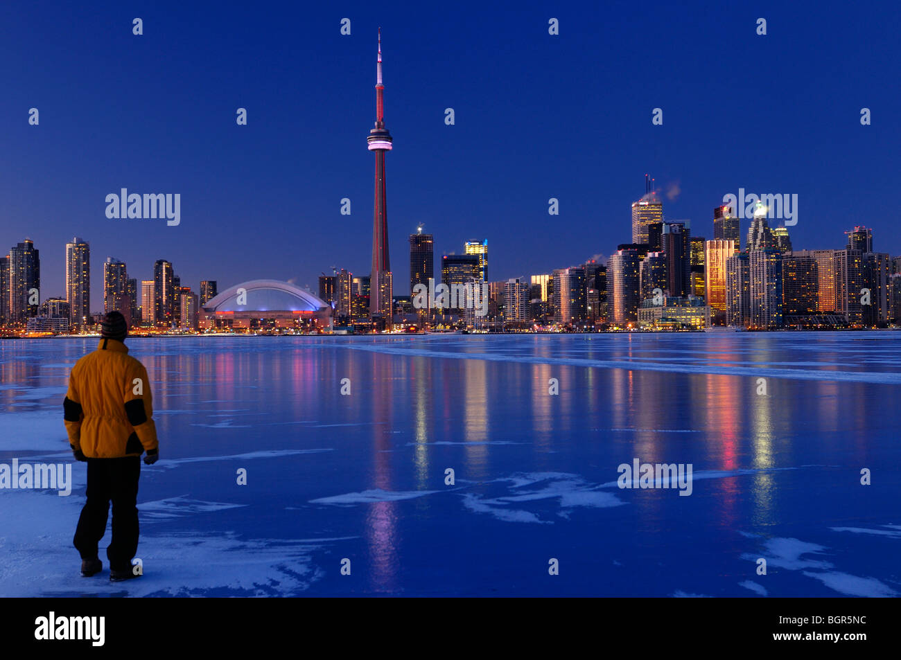 Uomo in piedi sul lago ghiacciato di ontario guardando toronto skyline della città luce fino al tramonto e riflettere su ghiaccio in inverno Foto Stock