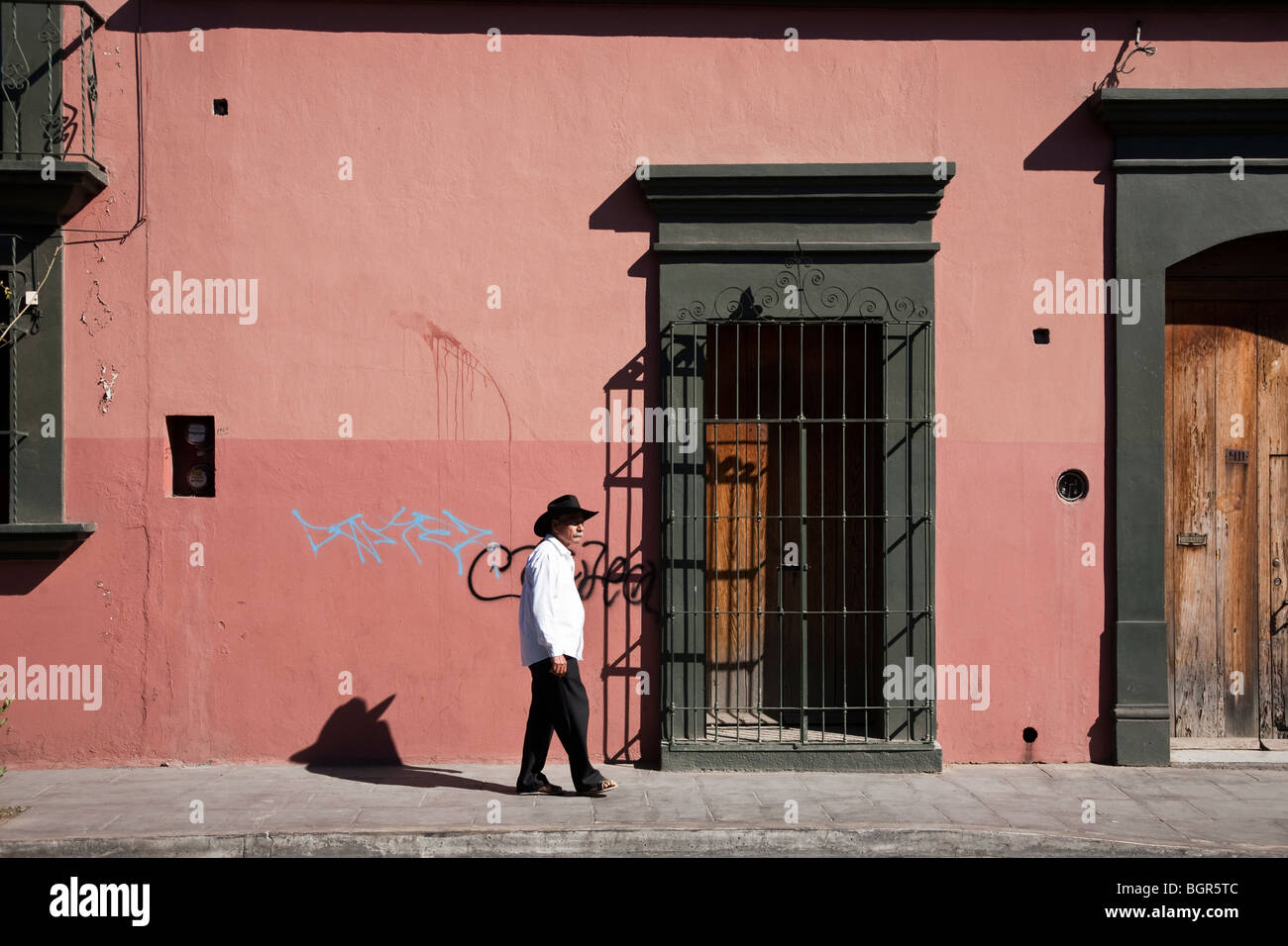 Il vecchio uomo con baffi bianchi vestita di nero sombrero passeggiate passato coloniale bellissimo edificio rifinito con rosa luminoso intonaco Foto Stock