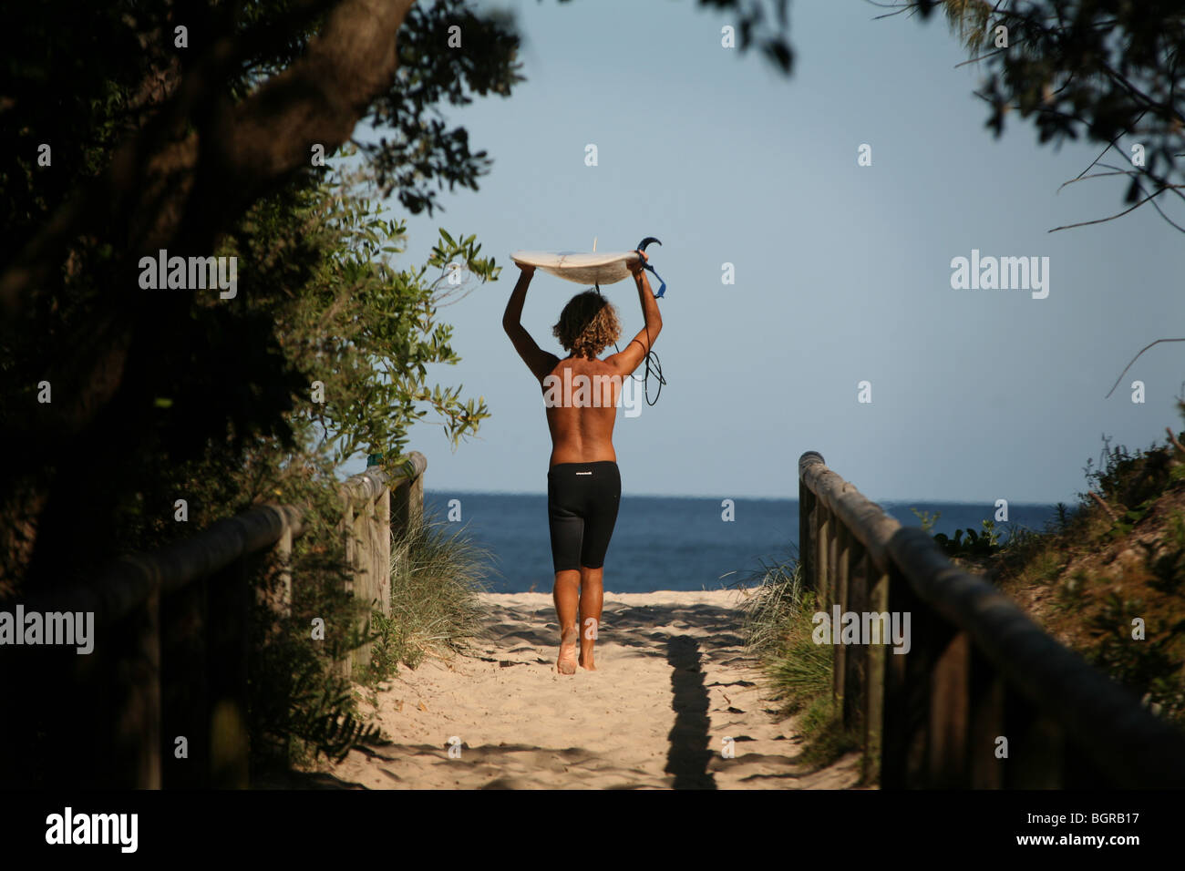 Un giovane uomo cammina per la spiaggia al Byron Bay con tavola da surf. Foto Stock