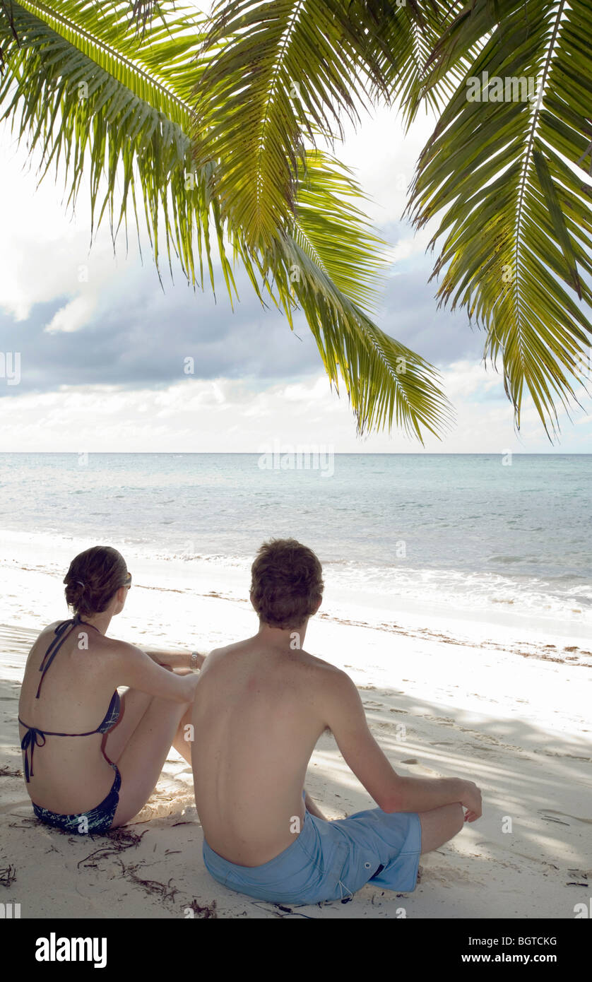 Coppia giovane seduto sulla spiaggia sotto le palme, Seicelle Foto Stock