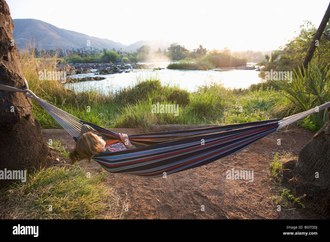 Giovane donna che dorme in una amaca accanto a Epupa Falls, fiume Kunene, Kaokoland, Namibia Foto Stock