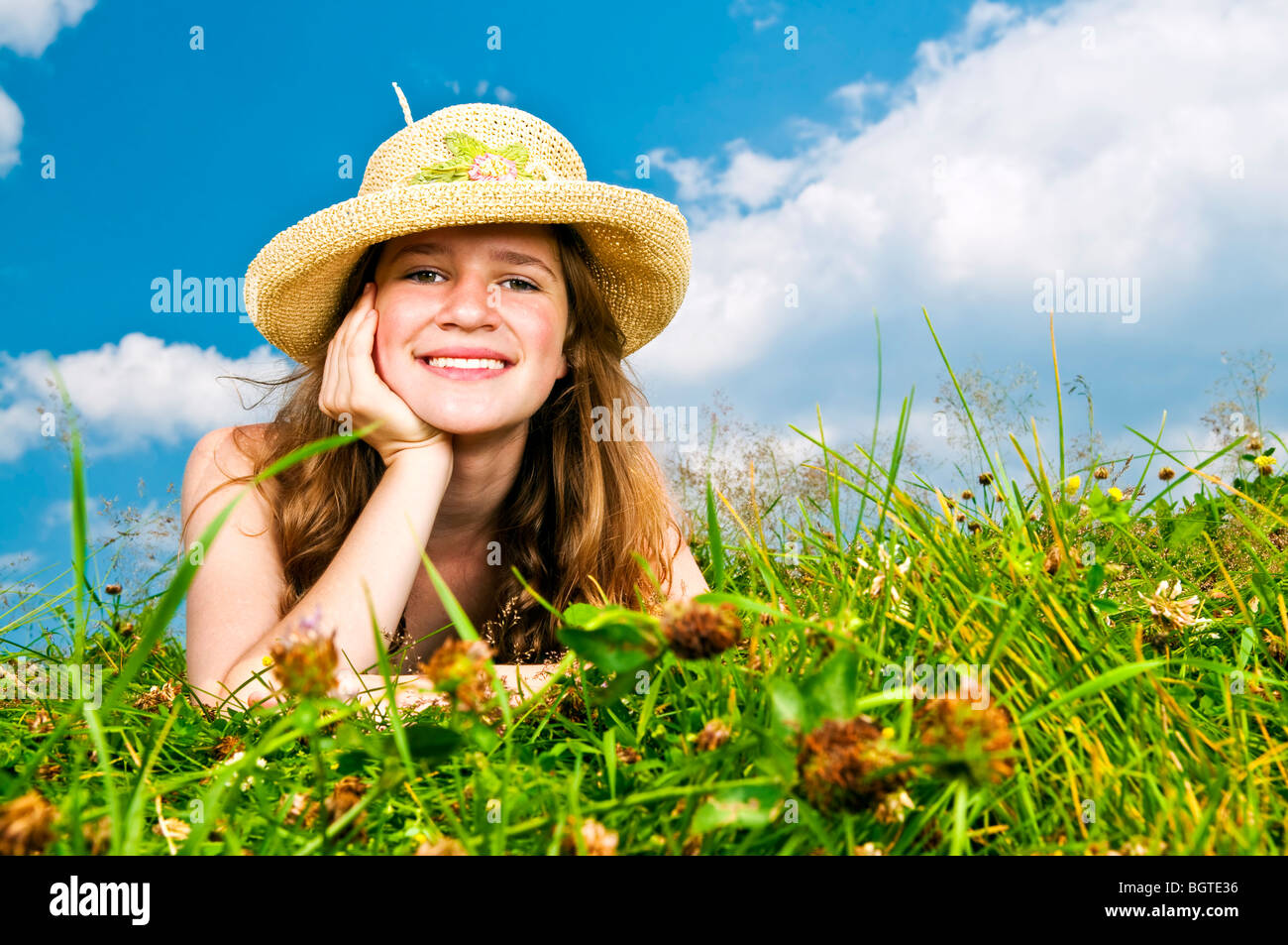 Giovane ragazza adolescente posa in prato estivo in appoggio il mento sulla mano nel cappello di paglia Foto Stock