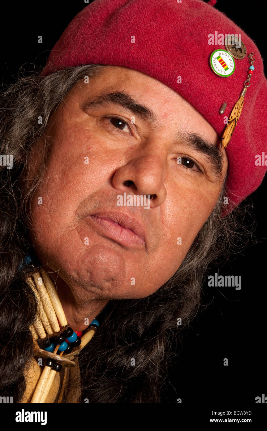Close up di native american indian Anishinabe maschio in Red Hat, medicina naturale uomo guaritore su sfondo nero con trecce Foto Stock