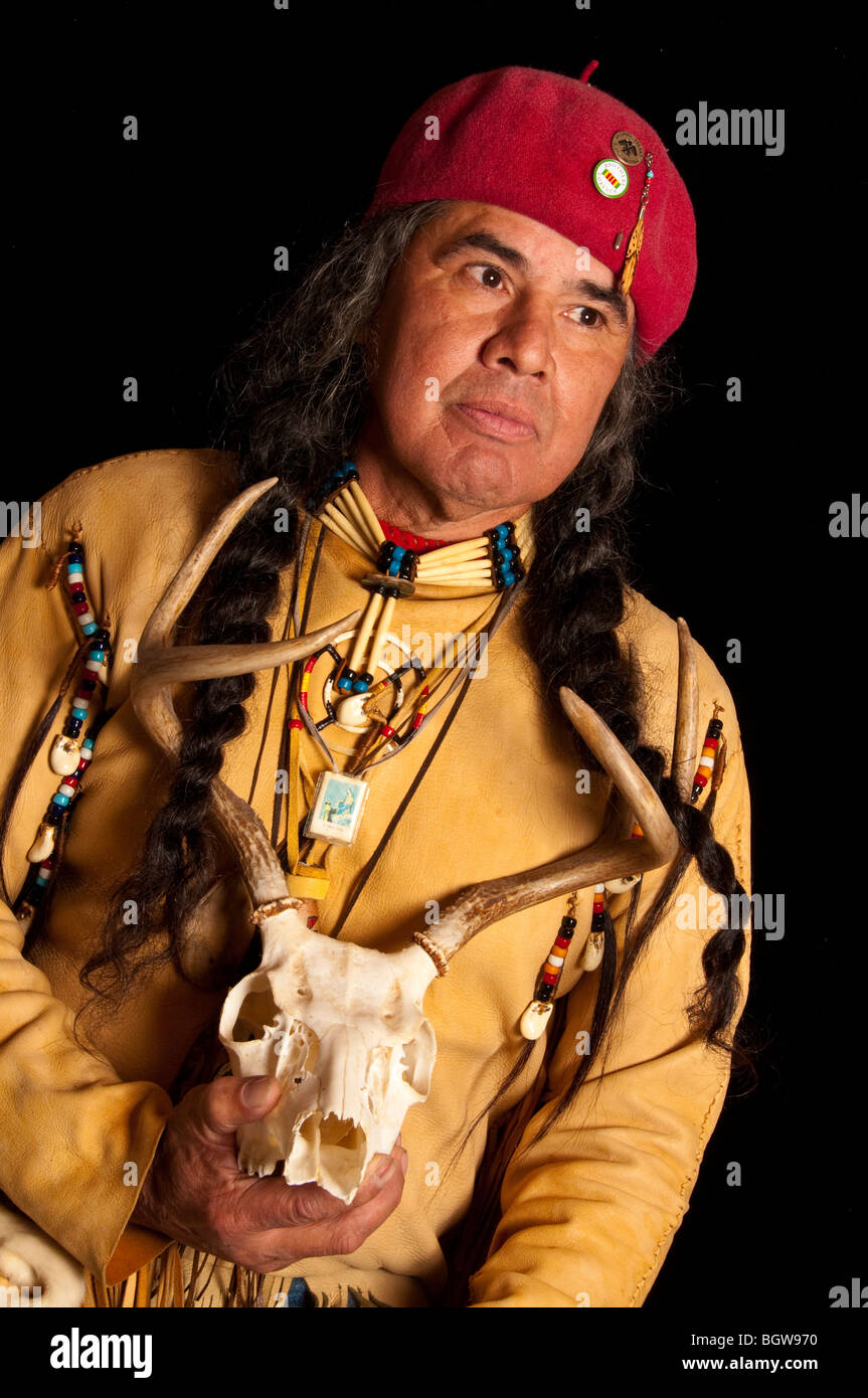 Native American Indian su sfondo nero con Red Hat lunghe trecce di indossare magliette di guarigione della pelle di cervo e il cranio di contenimento Foto Stock