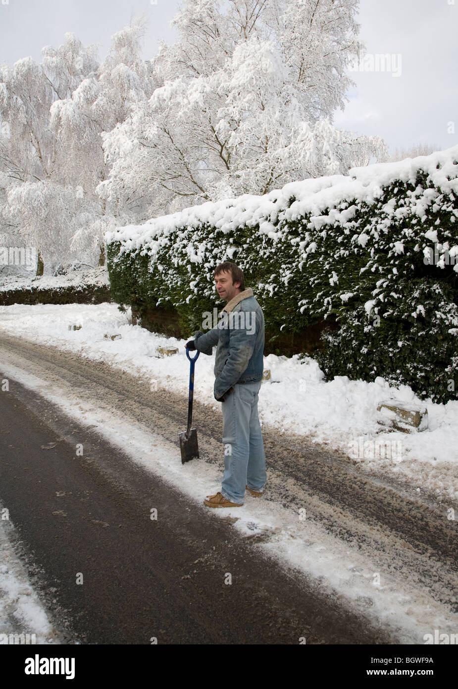 Uomo in piedi in strada con spade per cancellare neve pesante Foto Stock