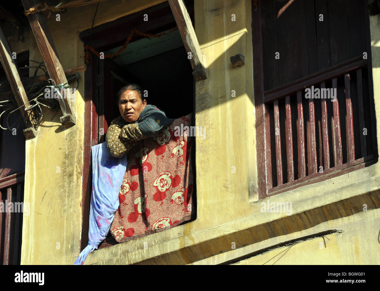 Donna nepalese staring giù in strada dalla finestra superiore Foto Stock