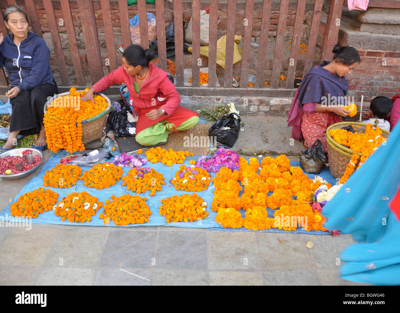 Donna street trader, vendendo le calendule, altri fiori da un foglio sulla strada nei pressi di Durbar Square, Kathmandu, Nepal. Foto Stock