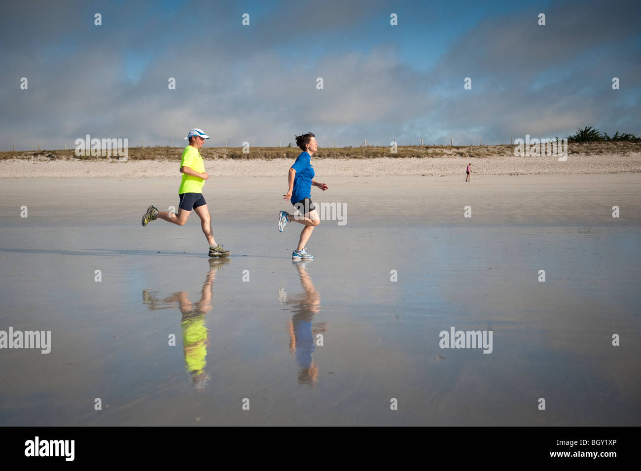 Due guide di scorrimento, le loro riflessioni nella sabbia bagnata, prendere un inizio di mattina correre lungo un piano di spiaggia di sabbia nel sud della Bretagna Foto Stock