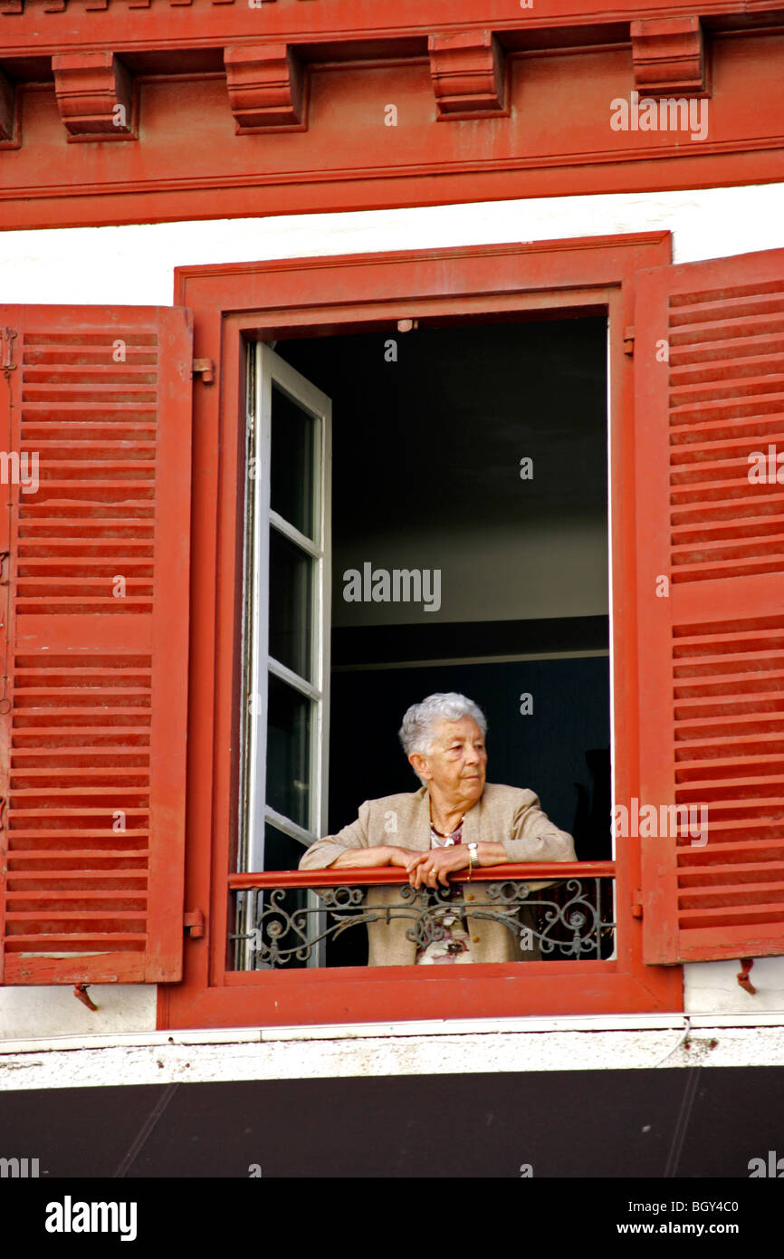 Donna anziana nella finestra persiane rosse St Jean de Luz port Bordeaux Costa Atlantica Aquitaine Francia Foto Stock